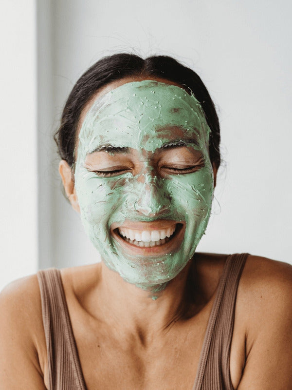 Smiling woman wearing a green layer of Mukti Deep Cleanse Enzyme Mask across her face.