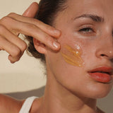 Woman massaging Mukti Gentle Melt Cleansing Balm onto her cheek beside the open jar.