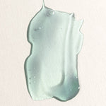 Translucent pale aqua gel spread into a thick, irregular swatch with small bubbles and raised edges on a textured cream background.