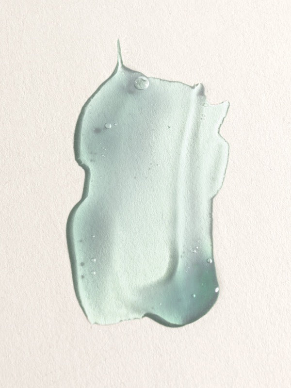 Translucent pale aqua gel spread into a thick, irregular swatch with small bubbles and raised edges on a textured cream background.
