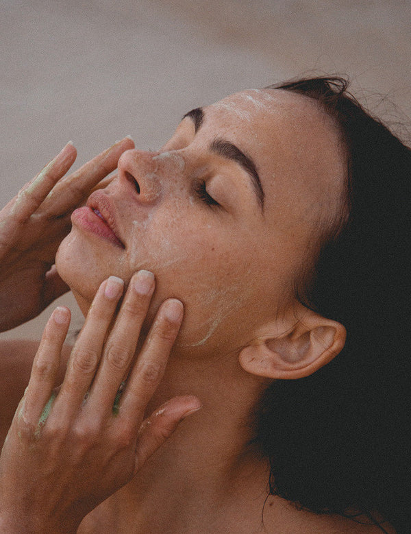 Woman relaxing with eyes closed while massaging Mukti 2-in-1 Resurfacing Exfoliant over her face.