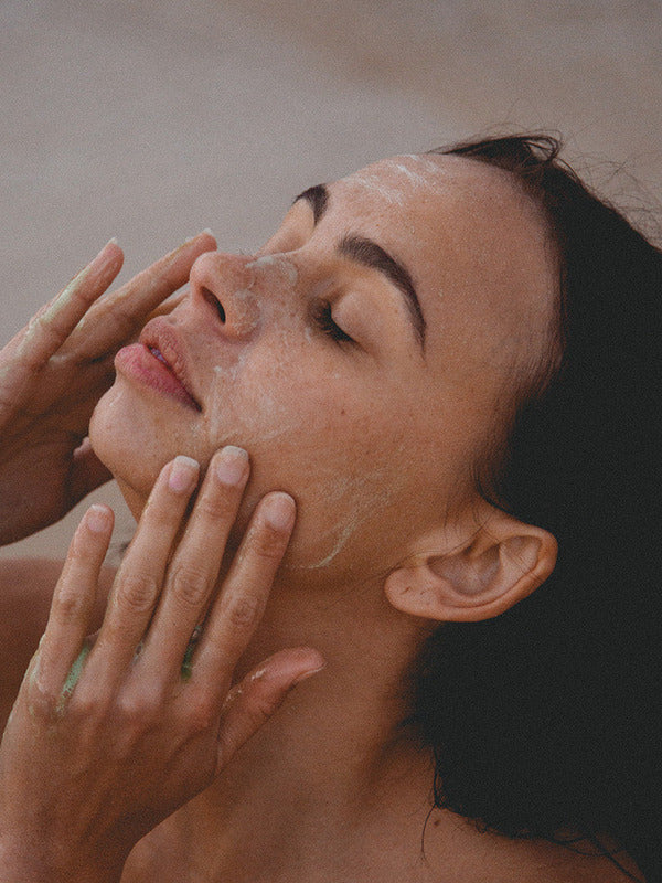 Woman relaxing with eyes closed while massaging Mukti 2-in-1 Resurfacing Exfoliant over her face.