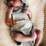 Newborn baby resting on a textured cream blanket while using an amber Natural Rubber Soother Small Rounded dummy.