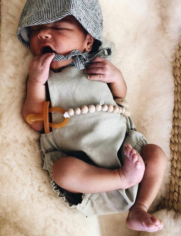 Newborn baby resting on a textured cream blanket while using an amber Natural Rubber Soother Small Rounded dummy.