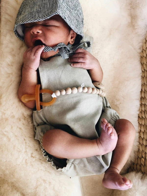 Newborn baby resting on a textured cream blanket while using an amber Natural Rubber Soother Small Rounded dummy.
