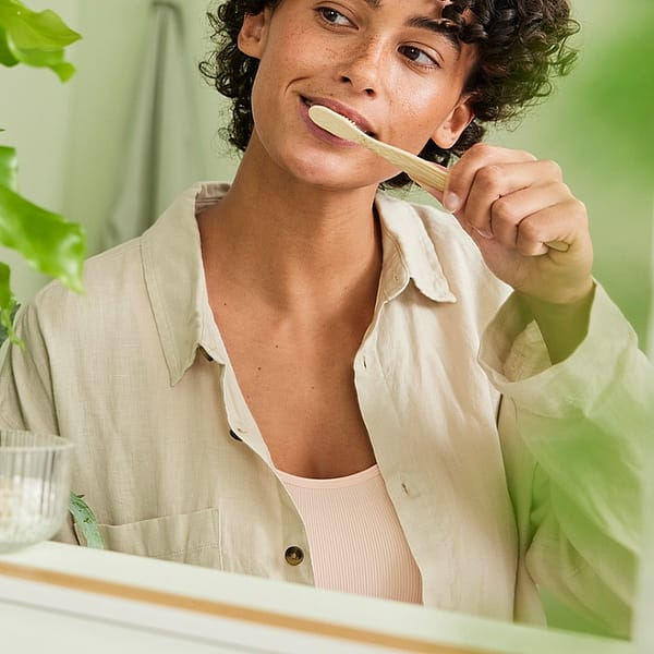 Dark skin woman with short curly hair brushing her teeth in front of the mirror.