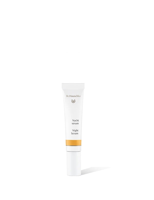 Small white Dr Hauschka Night Serum tube with a long white cap and a golden-yellow band, standing upright and casting a shadow to the right.