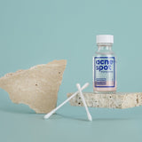 Noosa Basics Acne Spot Drying Lotion bottle styled with cotton buds and natural stone on a pale blue background.