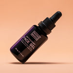 Dark Noosa Basics Antioxidant Face Oil bottle with a black dropper cap tilted diagonally against a peach background, casting a small shadow beneath it.