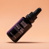 Dark Noosa Basics Antioxidant Face Oil bottle with a black dropper cap tilted diagonally against a peach background, casting a small shadow beneath it.
