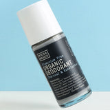 Clear Noosa Basics Charcoal and Eucalyptus roll-on deodorant bottle with a black label and white cap tilted diagonally against a pale blue background.