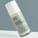 Clear Noosa Basics Lemon Myrtle roll-on deodorant bottle with a pale green label and white cap tilted diagonally against a grey-green background.