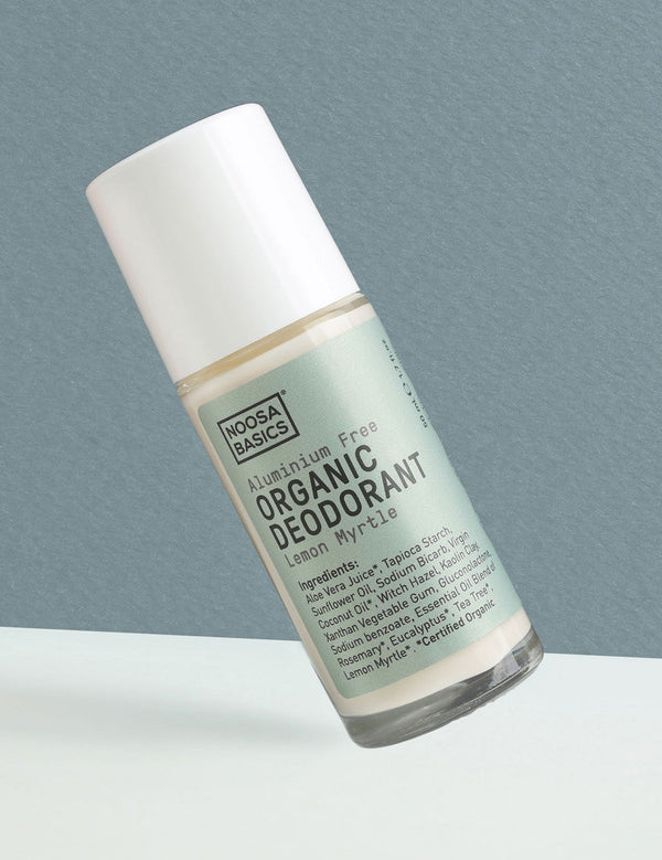 Clear Noosa Basics Lemon Myrtle roll-on deodorant bottle with a pale green label and white cap tilted diagonally against a grey-green background.