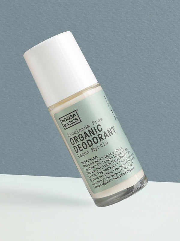 Clear Noosa Basics Lemon Myrtle roll-on deodorant bottle with a pale green label and white cap tilted diagonally against a grey-green background.