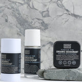 Noosa Basics Charcoal and Eucalyptus deodorant stick, roll-on bottle and square tin arranged beside a flat grey stone against a veined marble background, all with black labels.