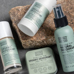 Noosa Basics Lemon Myrtle deodorant stick, roll-on bottle, spray and tin arranged across layered natural stones with the green-labelled stick resting diagonally in front.
