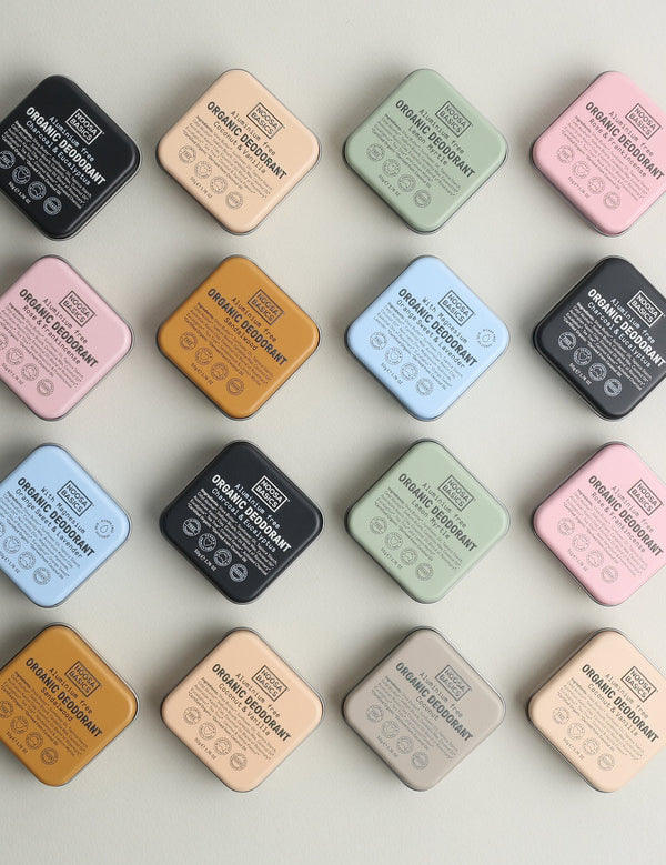 Sixteen square Noosa Basics deodorant tins arranged diagonally in a four-by-four grid, with black, peach, green, pink, orange, blue and beige lids facing upwards.
