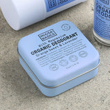 Close-up of pale blue Noosa Basics Sweet Orange and Lavender deodorants on a stone surface, with a square tin in front of a white stick container and a roll-on bottle.