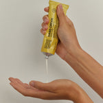 Hands squeezing a thin stream of white Noosa Basics Kakadu Plum and Vanilla Hand Cream from a yellow tube into an open palm.