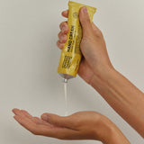 Hands squeezing a thin stream of white Noosa Basics Kakadu Plum and Vanilla Hand Cream from a yellow tube into an open palm.