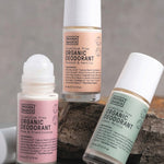 Three Noosa Basics roll-on deodorants arranged around a natural stone: Coconut and Vanilla, Lemon Myrtle, and Rose and Frankincense, with one roller ball exposed.