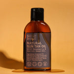 Amber Noosa Basics Natural Sun Tan Oil bottle with a black flip-top cap standing on an orange surface, surrounded by a small puddle of oil and casting a long shadow.