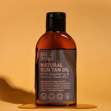 Amber Noosa Basics Natural Sun Tan Oil bottle with a black flip-top cap standing on an orange surface, surrounded by a small puddle of oil and casting a long shadow.