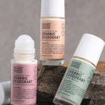 Three Noosa Basics roll-on deodorants arranged around a stone, including Rose and Frankincense, Lemon Myrtle, and Coconut and Vanilla.
