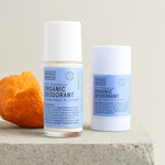 Noosa Basics Sweet Orange and Lavender deodorant stick and roll-on arranged on stone beside curled orange peel.
