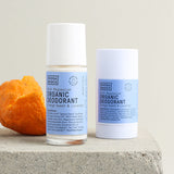 Noosa Basics Sweet Orange and Lavender deodorant stick and roll-on arranged on stone beside curled orange peel.