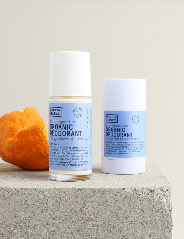 Noosa Basics Sweet Orange and Lavender deodorant stick and roll-on arranged on stone beside curled orange peel.