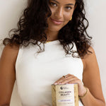 Woman in a white sleeveless top holding a jar of Nutra Naturals Collagen Beauty Vanilla at waist height against a neutral studio background.