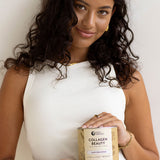 Woman in a white sleeveless top holding a jar of Nutra Naturals Collagen Beauty Vanilla at waist height against a neutral studio background.