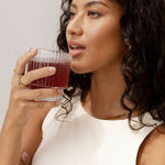 Lifestyle portrait of a woman holding a glass of red watermelon and strawberry drink for Nutra Organics Collagen Beauty Watermelon Strawberry.