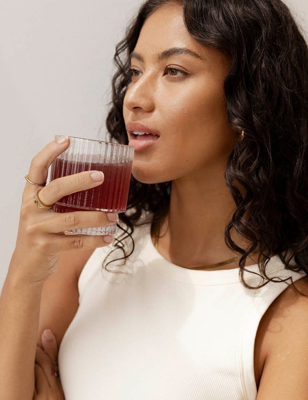 Lifestyle portrait of a woman holding a glass of red watermelon and strawberry drink for Nutra Organics Collagen Beauty Watermelon Strawberry.