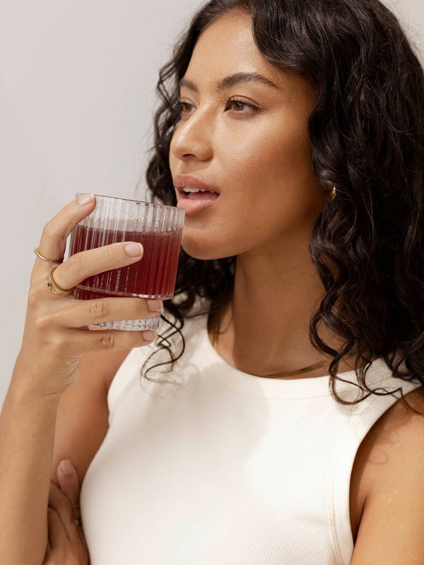 Lifestyle portrait of a woman holding a glass of red watermelon and strawberry drink for Nutra Organics Collagen Beauty Watermelon Strawberry.