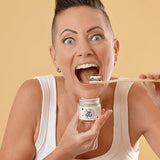 Woman holding Oh Gigi Flavour-Free Hydroxyapatite Tooth Powder and brushing her teeth