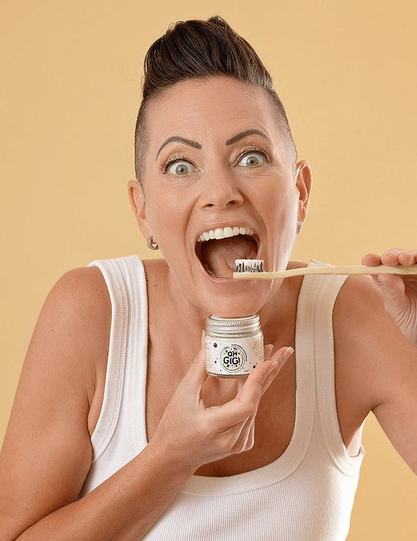 Woman holding Oh Gigi Flavour-Free Hydroxyapatite Tooth Powder and brushing her teeth