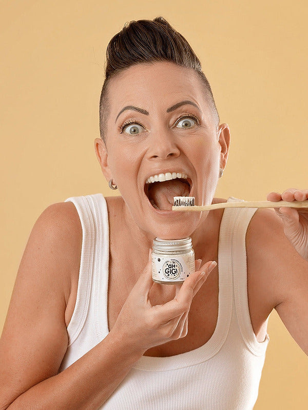 Woman holding Oh Gigi Flavour-Free Hydroxyapatite Tooth Powder and brushing her teeth