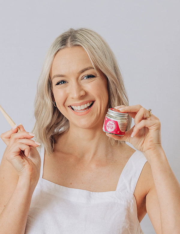 Woman smiling with a toothbrush and Oh Gigi Fruity Hydroxyapatite Tooth Powder