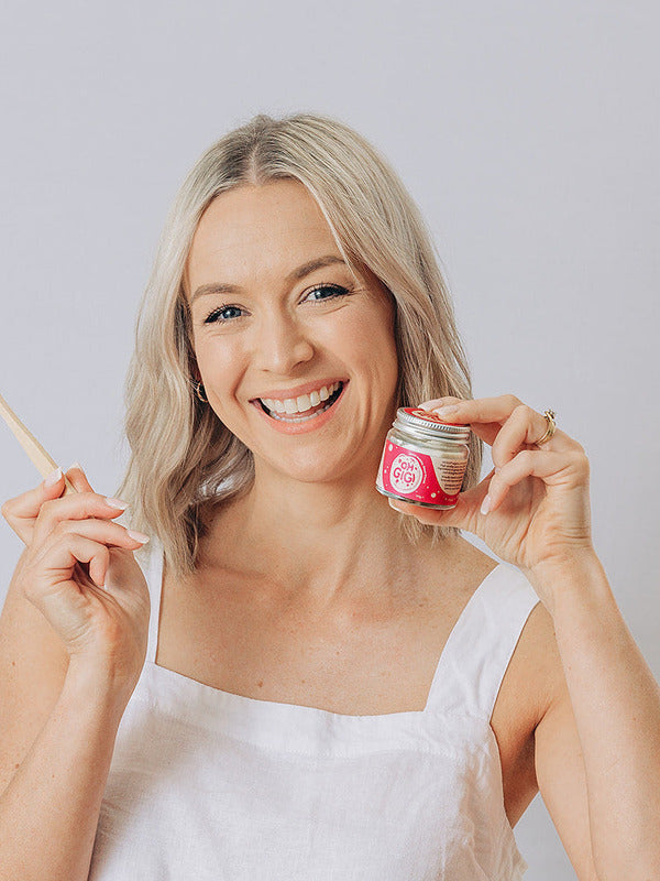 Woman smiling with a toothbrush and Oh Gigi Fruity Hydroxyapatite Tooth Powder