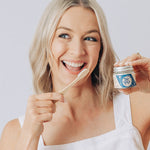 Woman smiling with a toothbrush and Oh Gigi Minty Hydroxyapatite Tooth Powder