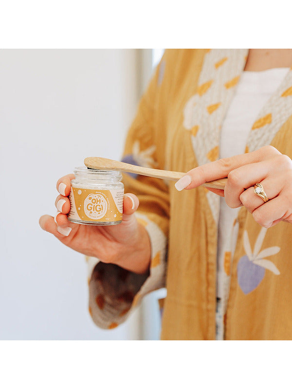 Person using Oh Gigi Native Hydroxyapatite Tooth Powder with a bamboo toothbrush