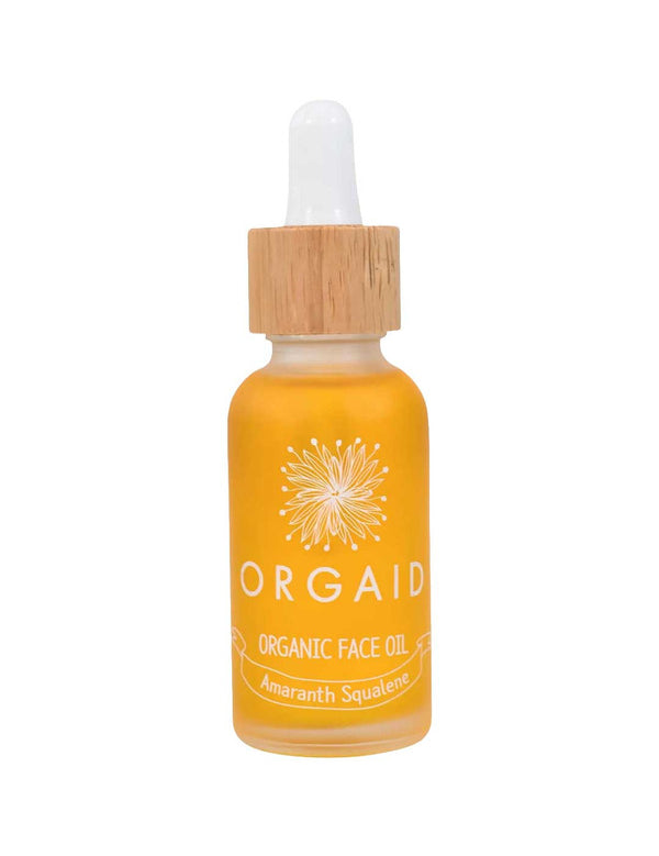 A 30ml glass bottle of Orgaid Organic Face Oil Amaranth Squalene with a wooden dropper cap contains yellow-orange amaranth squalene, features a white floral design, and has "Amaranth Squalene" labeled on the front.
