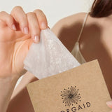 Woman removing an Orgaid Anti-Aging and Moisturising Organic Sheet Mask from its packet
