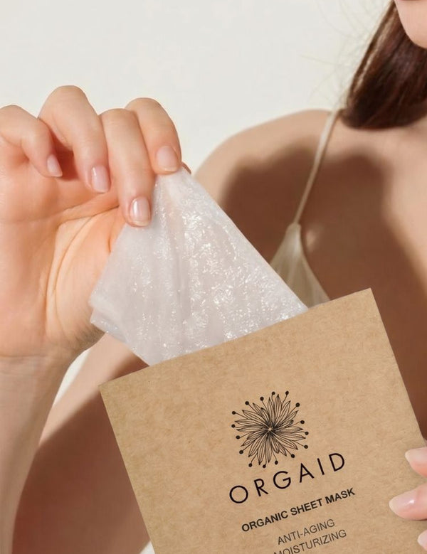 Woman removing an Orgaid Anti-Aging and Moisturising Organic Sheet Mask from its packet