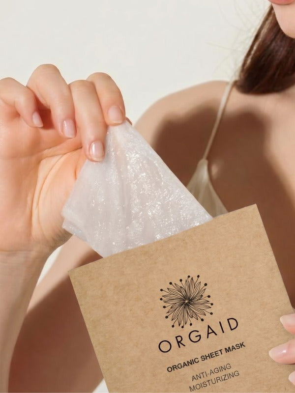 Woman removing an Orgaid Anti-Aging and Moisturising Organic Sheet Mask from its packet