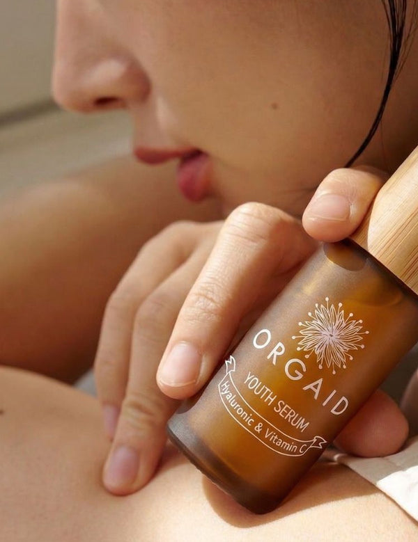 Woman holding Orgaid Youth Serum beside her face