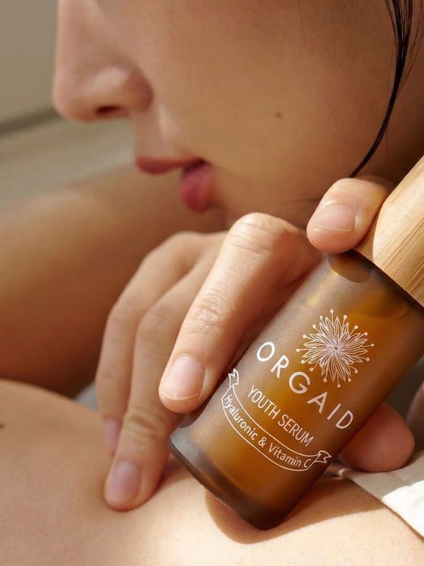 Woman holding Orgaid Youth Serum beside her face