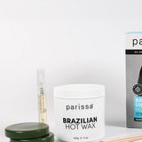 Three dark green wax discs stacked beside a white Parissa Brazilian Hot Wax jar, a slim tube and wooden spatulas, with the turquoise-panel box partly visible behind.